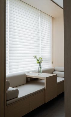 a vase with flowers sitting on a table in front of a window covered by blinds