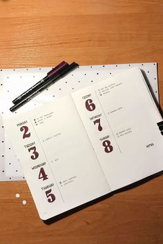 an open notebook on top of a wooden table next to a pen and paper with numbers