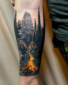 a man's arm with a fire and trees on it