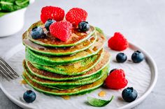 a stack of pancakes topped with berries and blueberries next to a bowl of raspberries