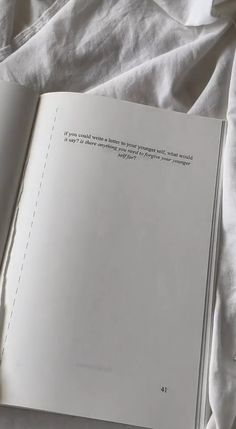 an open book sitting on top of a bed next to a white sheet and pillow