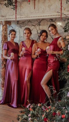 the bridesmaids pose with their champagnes in front of an arch decorated with flowers and greenery