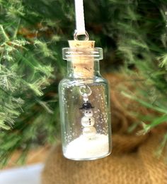 a snowman ornament in a glass bottle hanging from a christmas tree branch