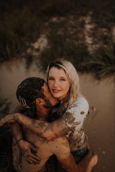 a man and woman hugging each other on the beach with mud all over their body