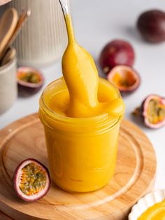 a small jar filled with yellow liquid on top of a cutting board next to sliced fruit