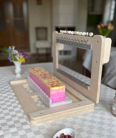 a pink and yellow cake sitting on top of a wooden tray next to a microwave oven