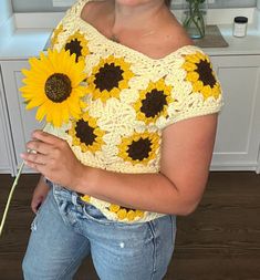 a woman holding a sunflower in her right hand and wearing a crochet top