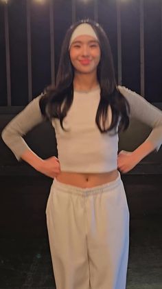 a woman standing with her hands on her hips wearing white pants and a crop top