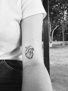 a small heart tattoo on the left inner arm, with a tree in the background