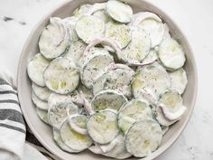 a white bowl filled with cucumbers and dill on top of a table