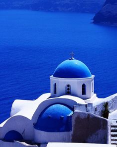 an image of a blue and white building overlooking the ocean in greece, with a red boat on it's side