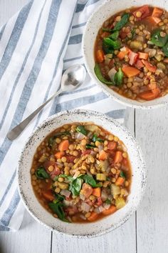 two bowls filled with soup sitting on top of a white wooden table next to a spoon