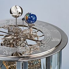 a silver clock with an earth globe on it's face and two pendulums in the middle