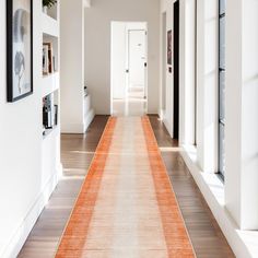 an orange runner rug is on the floor in front of white walls and framed pictures