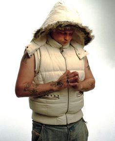 a man with tattoos wearing a white vest and holding a cell phone in his hands