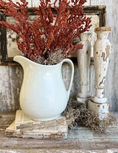 a white pitcher filled with red flowers on top of a wooden table