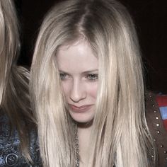 a woman with long blonde hair is looking at her cell phone while standing next to another woman