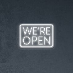 we're open neon sign in dark room with black wall and white flooring