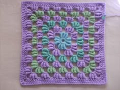 a crocheted square with green and purple flowers