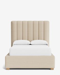 an upholstered bed with white pillows and beige linens on the headboard