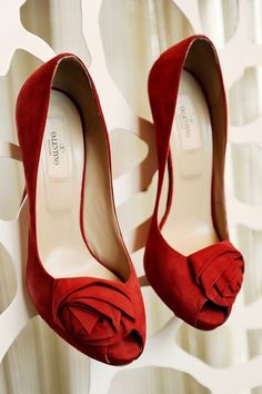 a pair of red high heels with a flower on the heel, hanging from a wall