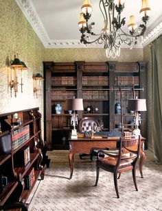 an old fashioned desk in the middle of a room with bookshelves and chandelier