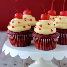 cupcakes with white frosting and cherries are on a cake platter