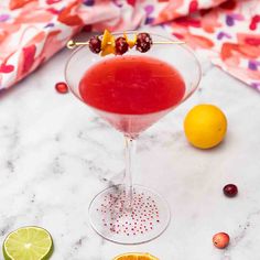 a drink in a martini glass garnished with cranberries and oranges