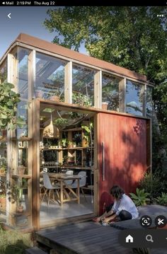 a person sitting on a wooden deck in front of a small building with glass walls