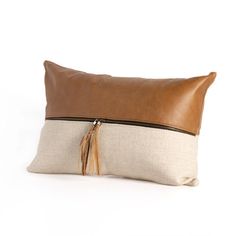 a brown and white pillow with tassels on the front, sitting on a white surface