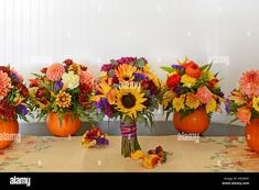 four pumpkins with flowers in them sitting on a table next to two vases