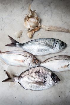 three fish are laying on the ground next to garlic