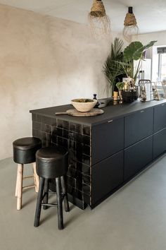 a kitchen with black cabinets and stools next to a potted plant on the counter