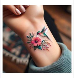 a woman's wrist tattoo with pink flowers and hummings on the back of her arm