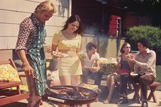 a group of people sitting around a bbq grill with food on it and one woman holding a plate