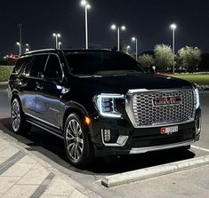 a black suv is parked in a parking lot at night with street lights behind it