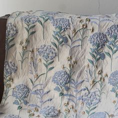 a blue and white flowered quilt on a couch with a wooden arm chair in the background