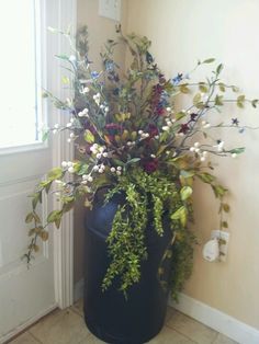 a black trash can with flowers and greenery in it sitting next to a door