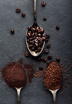 two spoons filled with coffee beans and ground coffee on a dark surface next to them