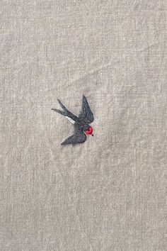 a small bird with a red heart in its beak on a light gray linen background