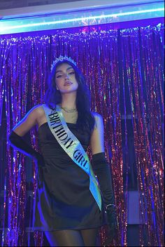 a woman wearing a tiara standing in front of a purple curtain with sequins on it