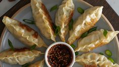 a white plate topped with dumplings covered in sauce next to a bowl of dipping sauce