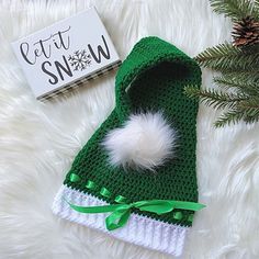 a green and white knitted hat next to a pine tree