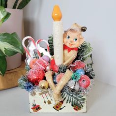 a christmas decoration with a candle and ornaments in the shape of a boy sitting on top of a box