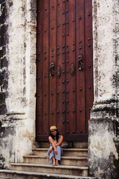 a woman sitting on the steps in front of a door with a hat on her head