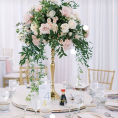 a tall vase with flowers and greenery is on top of a white table cloth