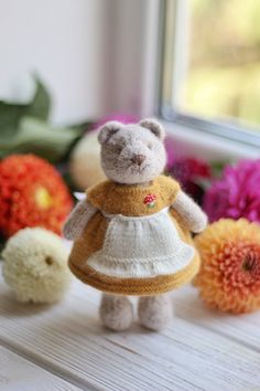 a teddy bear in a dress next to flowers