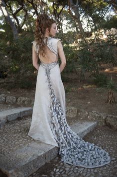 a woman with long hair wearing a white dress and chain around her neck standing on some steps