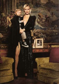 a woman in a black dress holding a baby and posing for a photo with a painting behind her