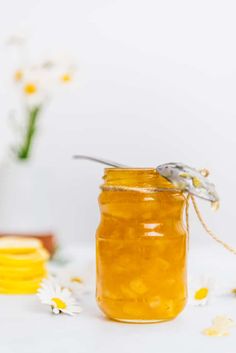 a jar filled with honey sitting on top of a table next to some daisies